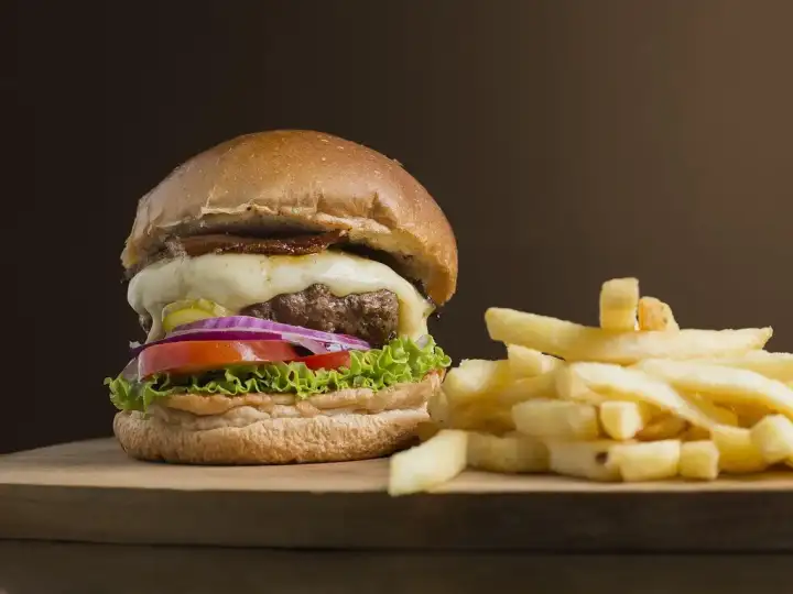 Burger in Wien: Burger mit Käse, Salat, Tomate und roten Zwiebeln neben Pommes auf einem Holzbrett