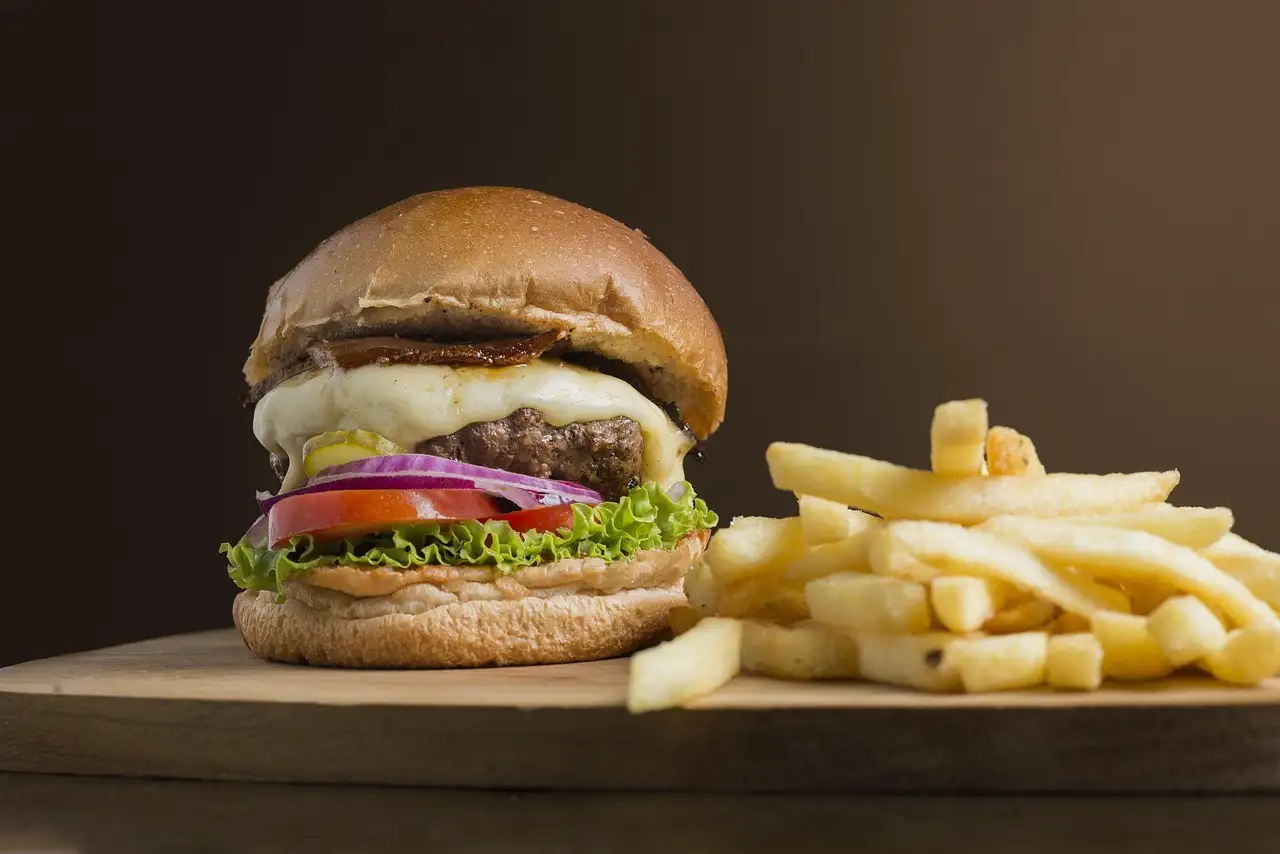 Burger in Wien: Burger mit Käse, Salat, Tomate und roten Zwiebeln neben Pommes auf einem Holzbrett