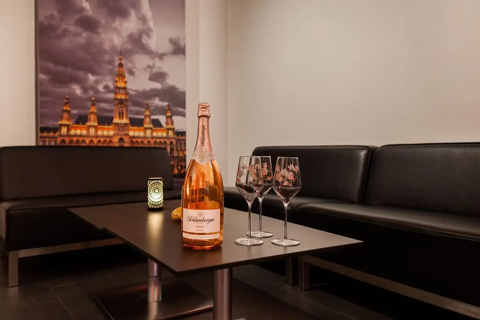 Lounge mit schwarzen Ledersofas, Flasche Schlumberger Rosé und drei Gläsern vor Rathaus-Bild