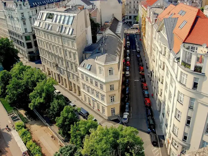 Wien Bezirke: Blick von oben auf eine Straße mit hellen Altbauten, Dachgauben, Bäumen und parkenden Autos