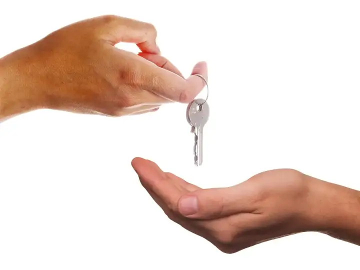 Wohnungssuche Wien: Eine Hand übergibt einen Schlüssel an eine offene Hand vor weißem Hintergrund